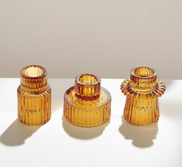 A set of three amber-colored glass candle holders with vertical stripes, arranged in different sizes on a neutral background.