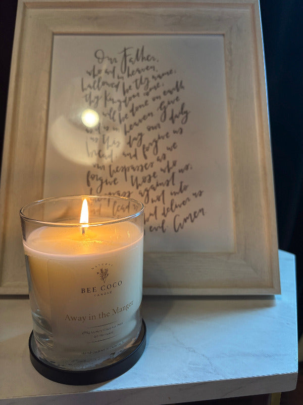 Away in the Manger candle lit and displayed in front of a framed print of the "Our Father" prayer