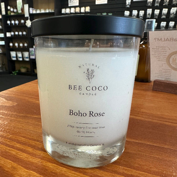 Candle labeled 'Bee Coco Bobo Rose' on a wooden surface with a blurred background