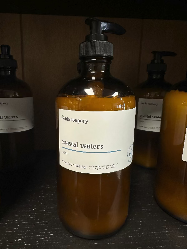 A glass pump bottle of body lotion labeled 'coastal waters' from The Noble Soapery.
