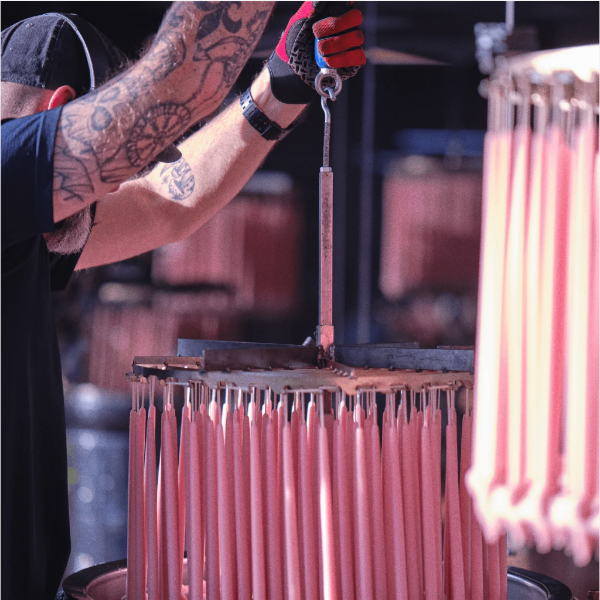 worker hand dipping beeswax tapers