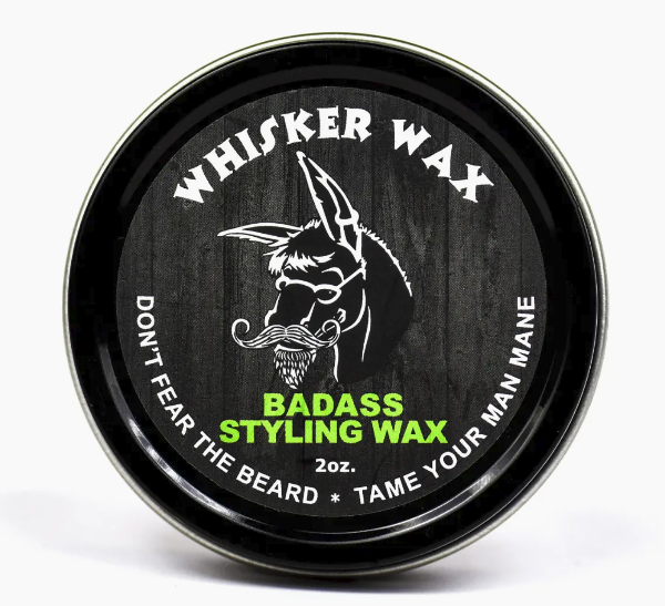 A container of 'Whisker Wax' branded as 'BADASS STYLING WAX' with a graphic of a donkey wearing a mustache. The container is black with a lid, and the label has white and green text.