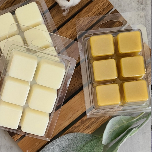 Packaged wax melts on a wooden surface with cotton and greenery.