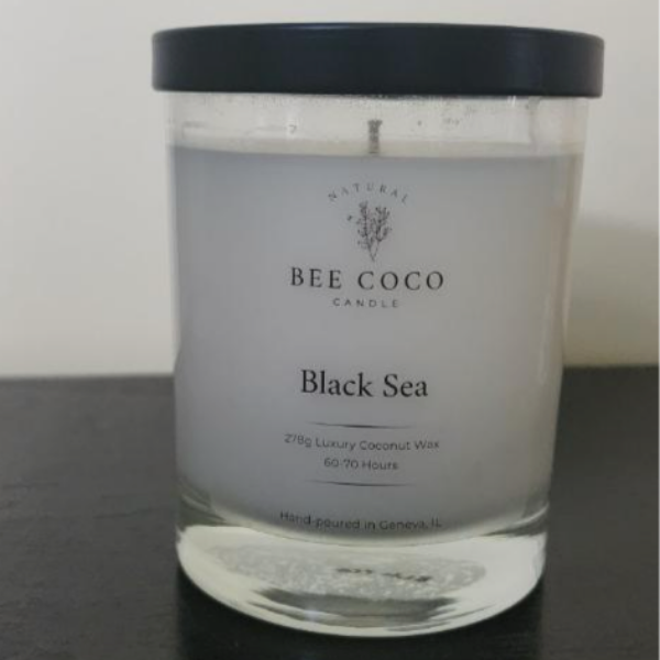 A clear glass candle jar with a black lid, labeled 'Black Sea' from Bee Coco Candle, indicating a luxury coconut wax candle with a burn time of 60-90 hours.