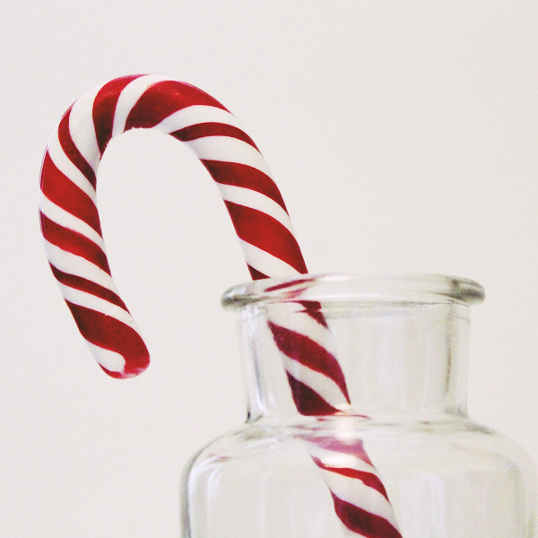 A candy cane placed inside a clear glass jar, representing the product 'Candy Cane Swirl Melts' from Bee Coco Candle.