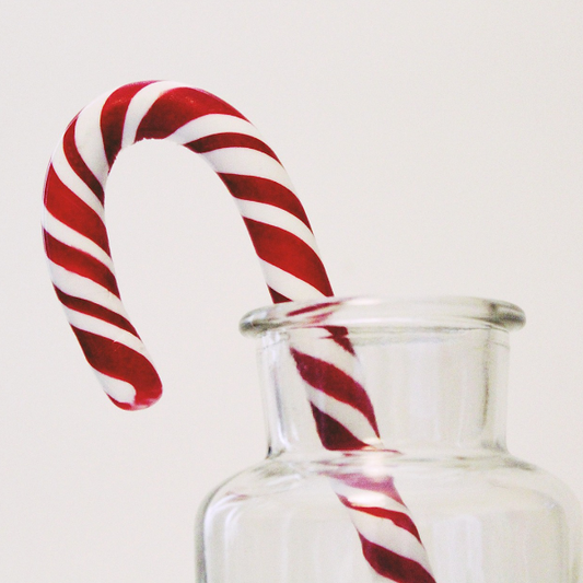 A candy cane placed inside a clear glass jar, representing the product 'Candy Cane Swirl Melts' from Bee Coco Candle.