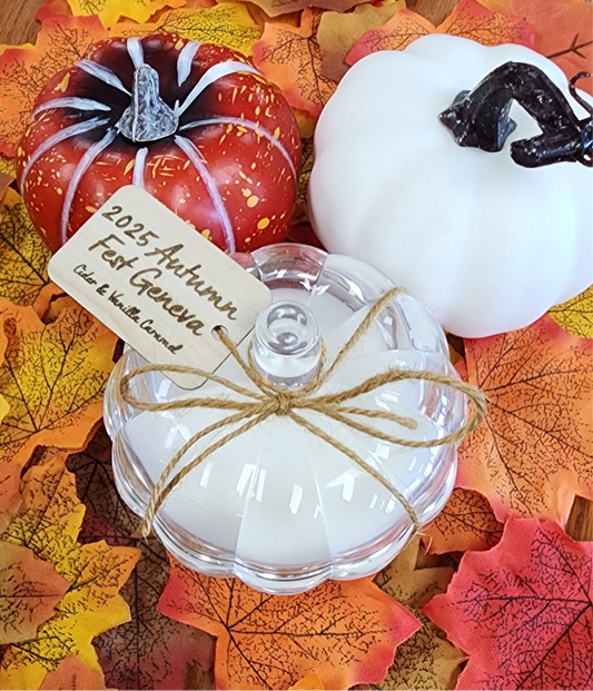Pumpkin-shaped candle with a label on a bed of autumn leaves