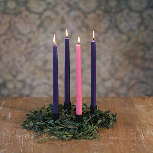 Four candles in purple and pink on a green wreath against a patterned wall.