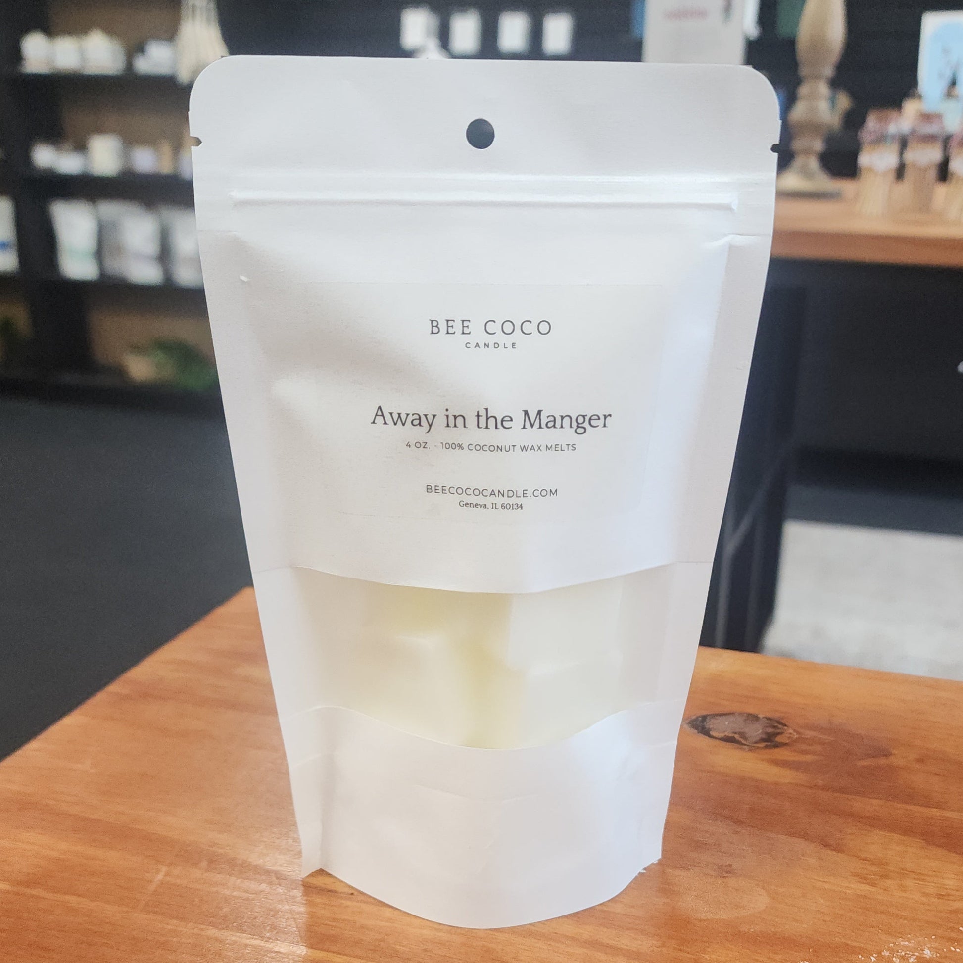 White packaging of BEE COCO candles on a wooden surface with a blurred background