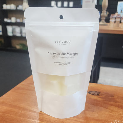 White packaging of BEE COCO candles on a wooden surface with a blurred background