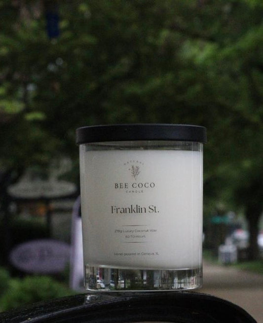 A white candle with a black lid labeled 'Franklin St.' by Bee Coco.