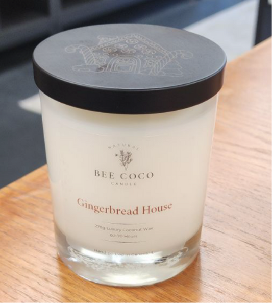 A scented candle with a label reading 'Gingerbread House' from Bee Coco Candle, placed on a wooden surface.