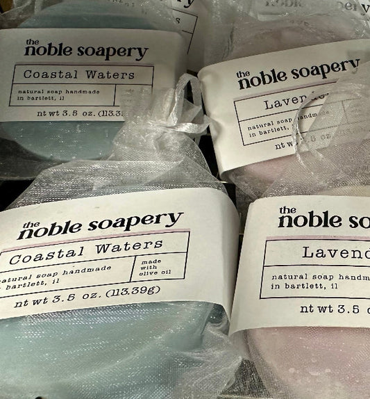 Multiple bars of soap from 'the noble soapery' with labels on a white background.