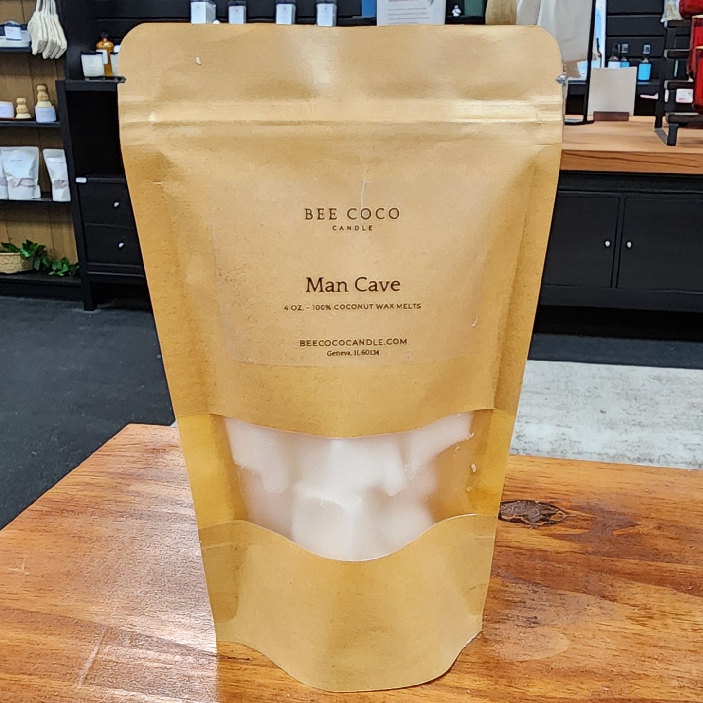 Bee Coco Man Cave candle packaging on a wooden table with a store interior in the background.