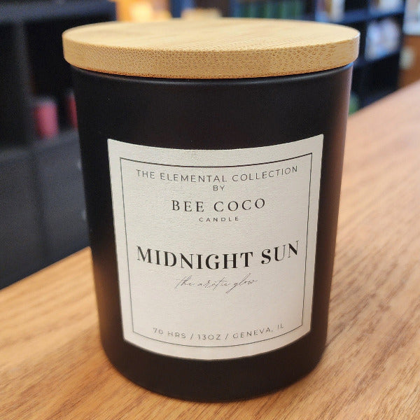 Candle labeled 'Midnight Sun' by Bee Coco Candle on a wooden surface with blurred background