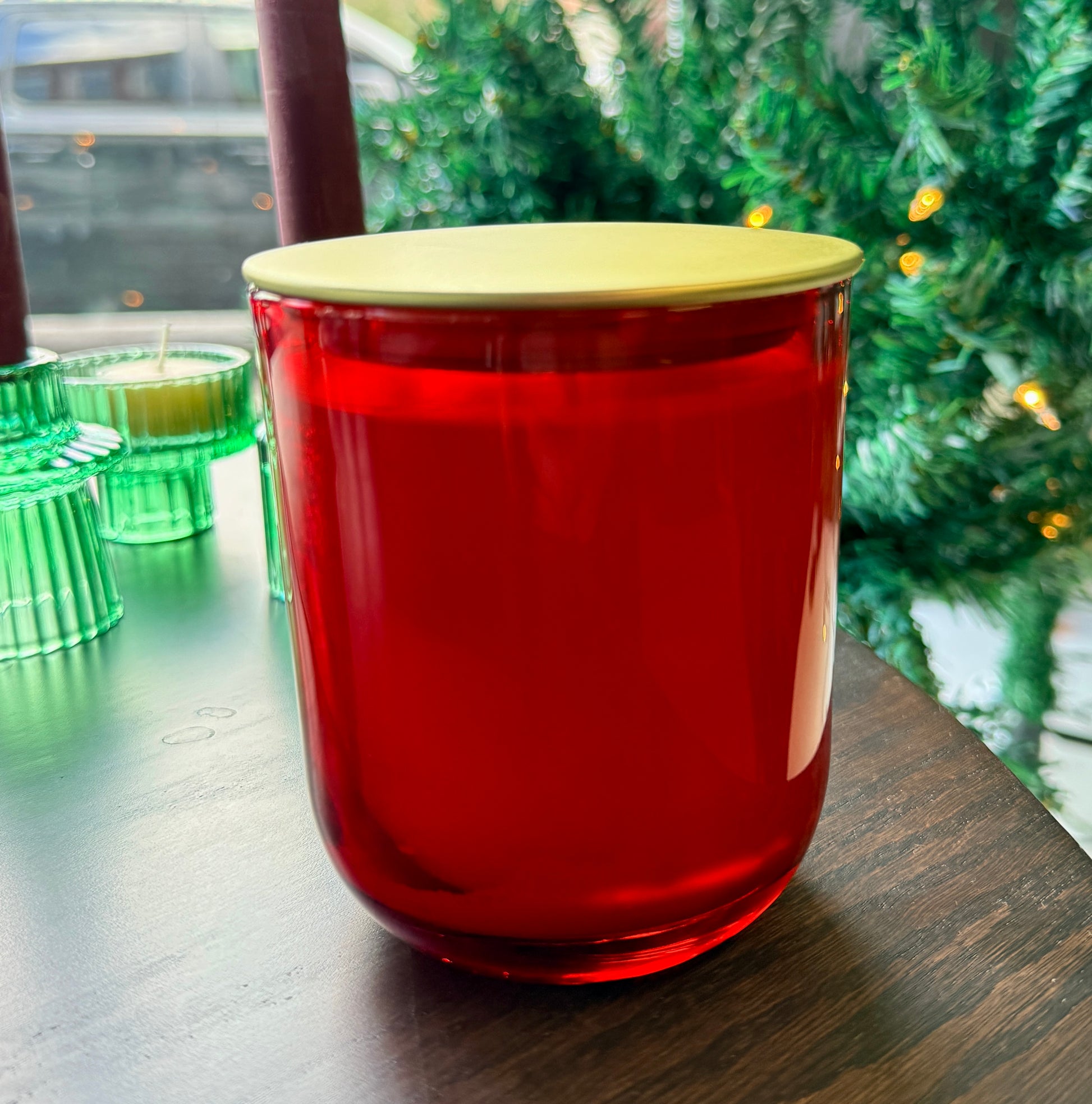 Red candle with a gold lid on a table with green candles in the background.