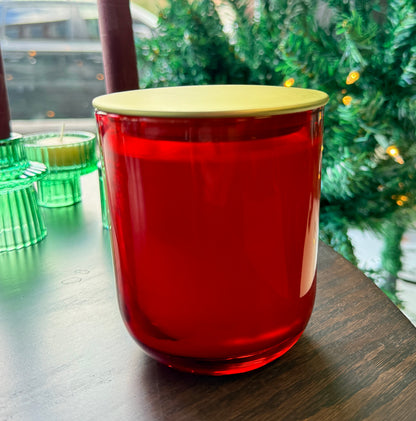 Red candle with a gold lid on a table with green candles in the background.