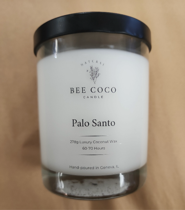 A white candle in a clear glass jar with a black lid, labeled 'Palo Santo' from Bee Coco Candle.