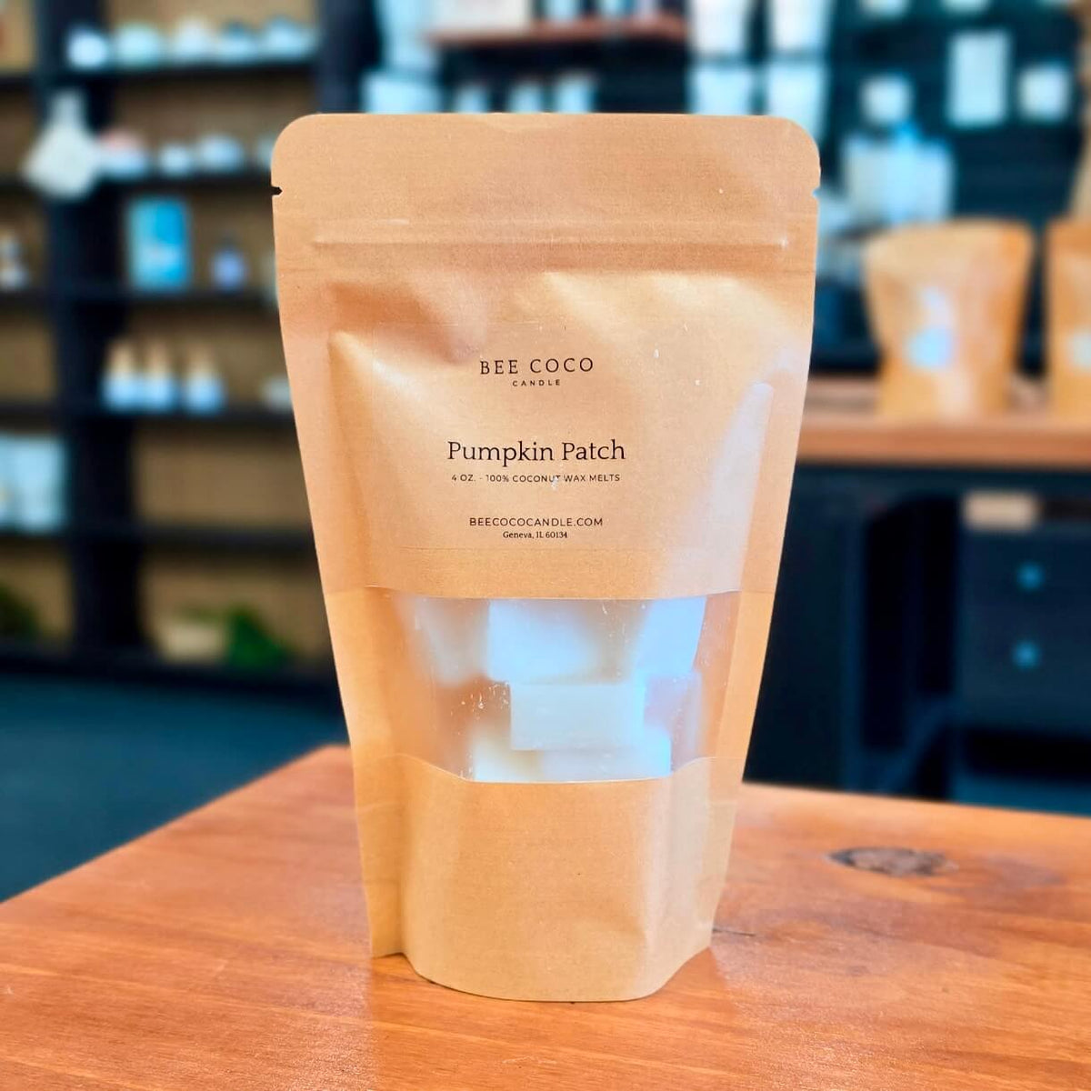 A kraft paper stand-up pouch labeled 'BEE COCO CANDLE Pumpkin Patch' sits on a wooden table with a softly blurred indoor background.
