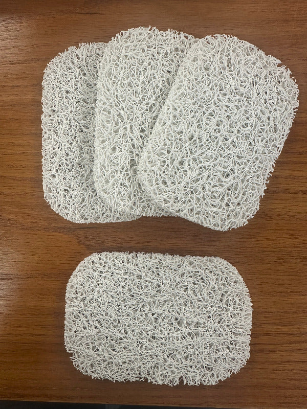 Four white mesh soap savers laid out on a wooden surface.