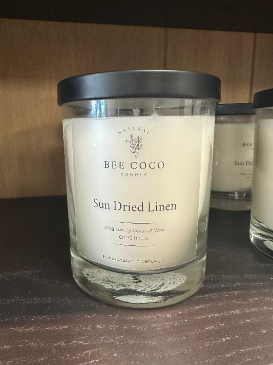 A clear glass jar candle with a black lid, labeled 'Sun Dried Linen', from Bee Coco Candle.