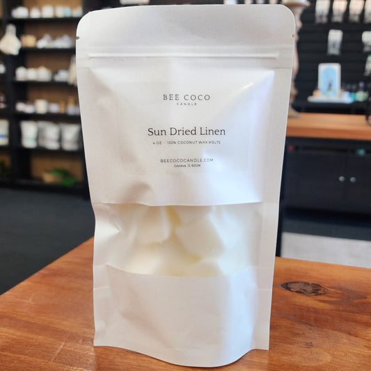 White packaging of BEE COCO candles on a wooden surface with a blurred store background