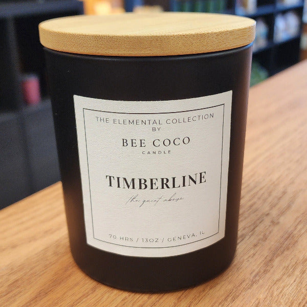 Timberline candle by Bee Coco Candle on a wooden surface with a blurred background.