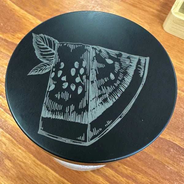 Black container lid with white fruit illustration on a wooden surface