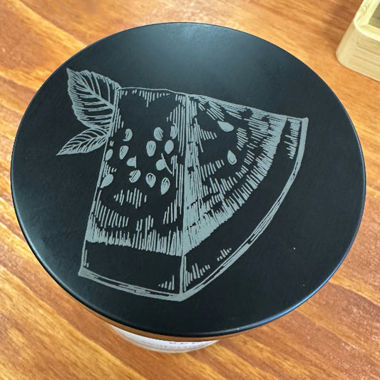 Black container lid with white fruit illustration on a wooden surface