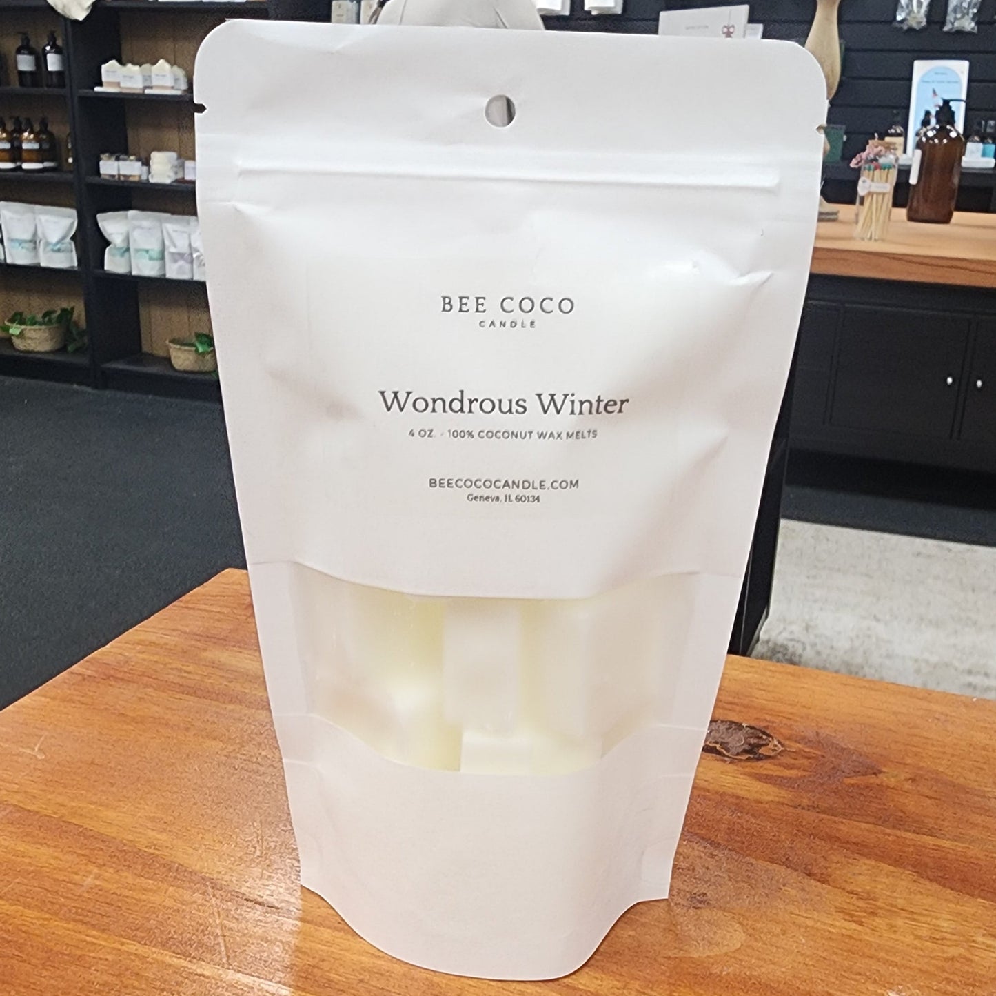 White packaging of BEE COCO candle labeled 'Wondrous Winter' on a wooden surface.