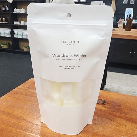 White packaging of BEE COCO candle labeled 'Wondrous Winter' on a wooden surface.