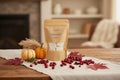 A kraft paper pouch labeled 'MELSCO Cranberry Harvest' stands on a white cloth on a wooden table, surrounded by cranberries, small pumpkins, dried grass, and autumn leaves in a softly blurred indoor setting.