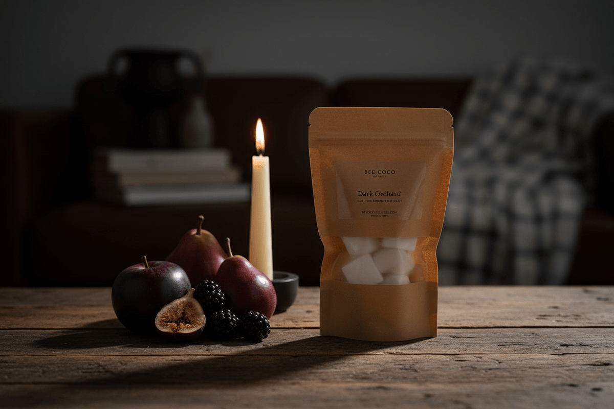 A kraft paper stand-up pouch labeled ' Dark Orchard' sits on a rustic wooden table beside a lit candle, pears, an apple, and blackberries in a dimly lit indoor setting.