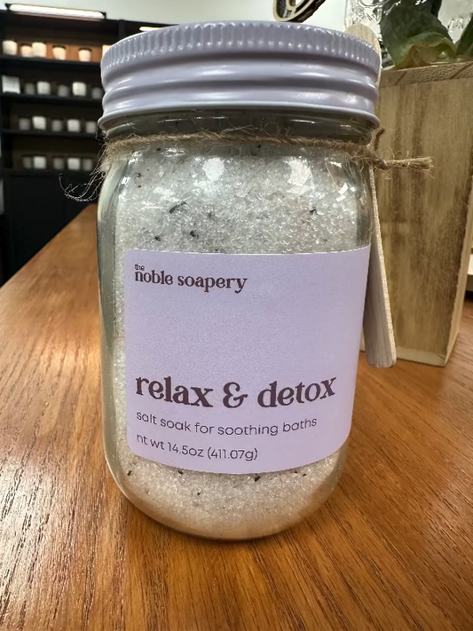 A jar of 'Relax & Detox' bath salts by The Noble Soapery, with a white label on a wooden surface.
