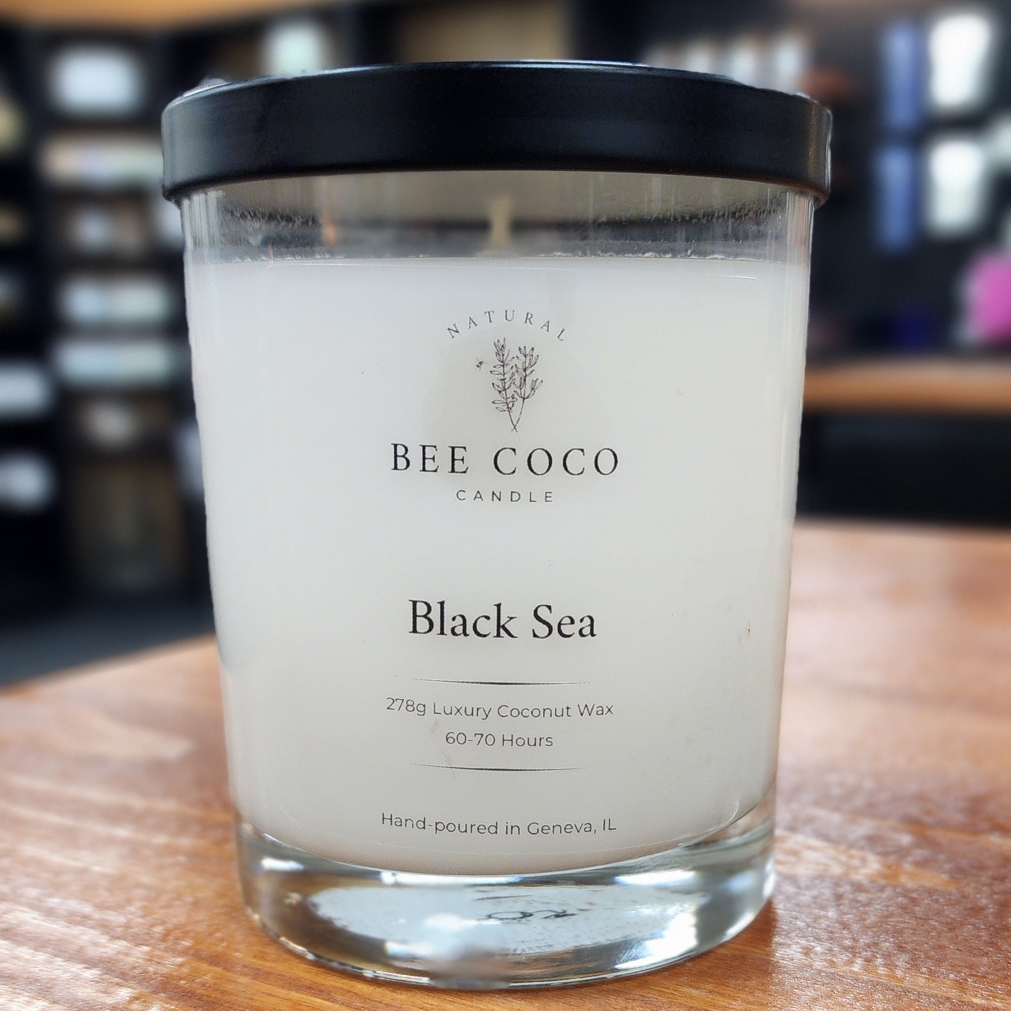 Candle labeled 'Black Sea' by 'Bee & Coco' on a wooden surface.