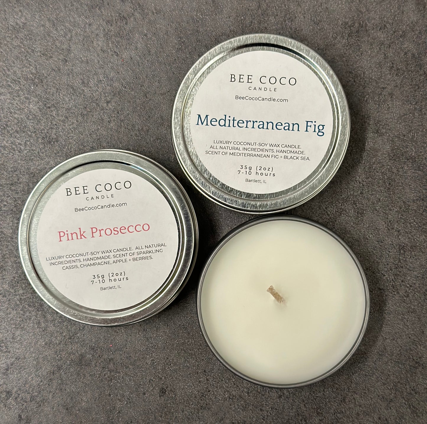 Three travel tins labeled 'BEE COCO CANDLE' in different scents such as Mediterranean Fig, Pink Prosecco, and Coco Beach, with the candles visible and the tins describing the scent as '100% natural coconut wax infused with essential oils'.